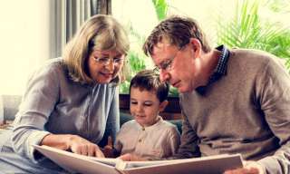 Grosseltern mit ihrem Enkel in der Mitte erzählen ein Buch.
