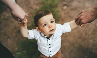 Ein kleiner Junge hält die Hände seiner Eltern und schaut zur Kamera.